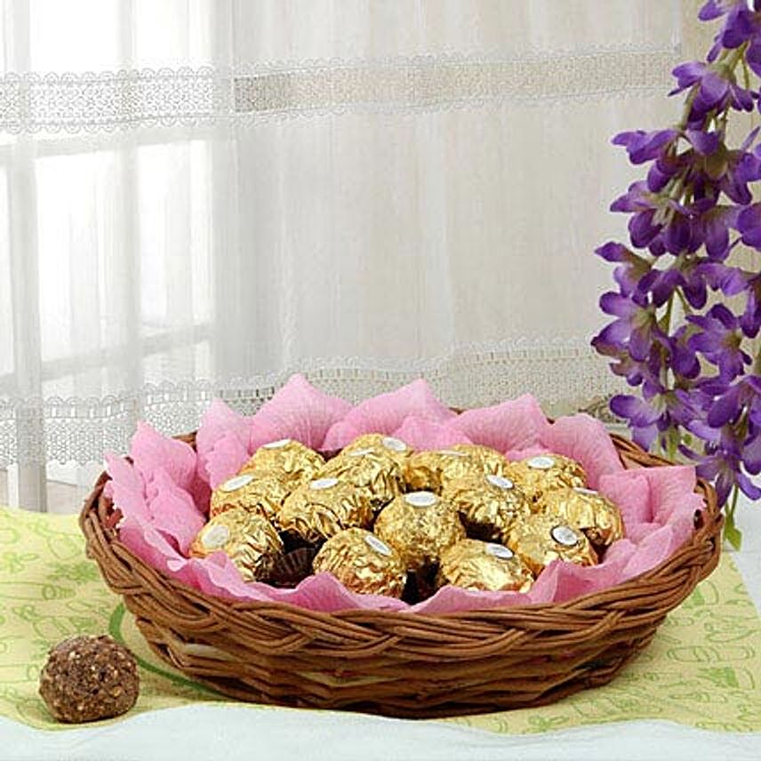 Ferrero rocher chocolates and artificial pink paper petals in a round cane basket:Gift Baskets to Ludhiana