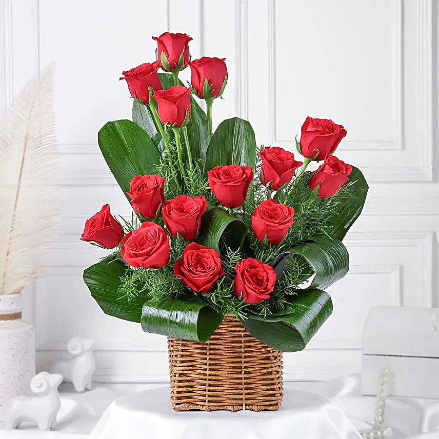 Cane basket arrangement of 15 red roses, draceane leaves and seasonal filler
