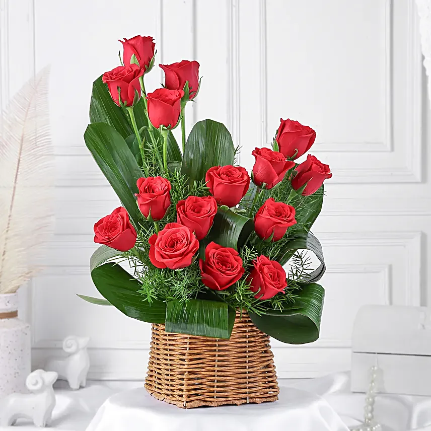 Cane basket arrangement of 15 red roses, draceane leaves and seasonal filler