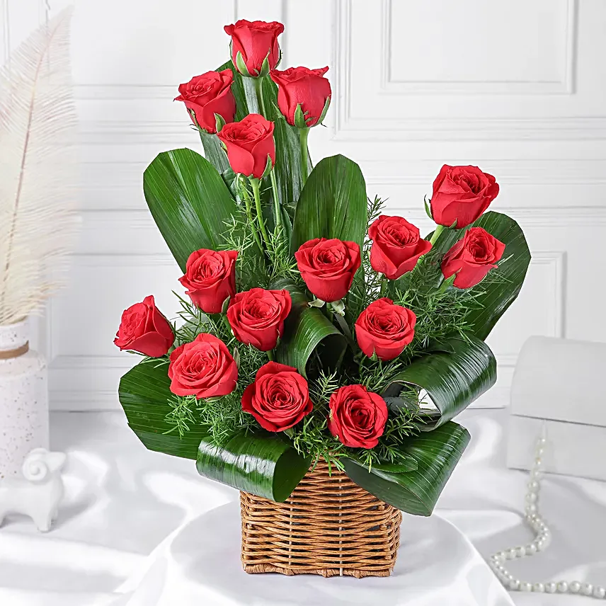 Cane basket arrangement of 15 red roses, draceane leaves and seasonal filler