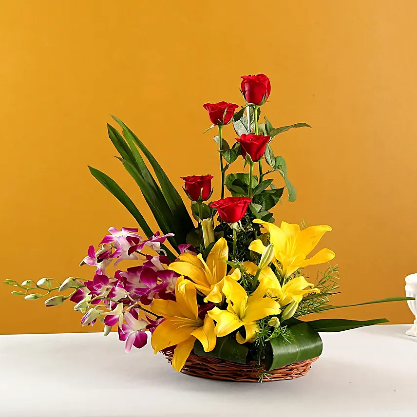 Cane basket arrangement of 5 red roses, 4 purple orchids, 2 yellow asiatic lilies and draceane leaves