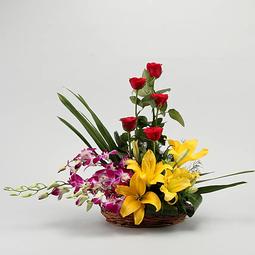 Cane basket arrangement of 5 red roses, 4 purple orchids, 2 yellow asiatic lilies and draceane leaves
