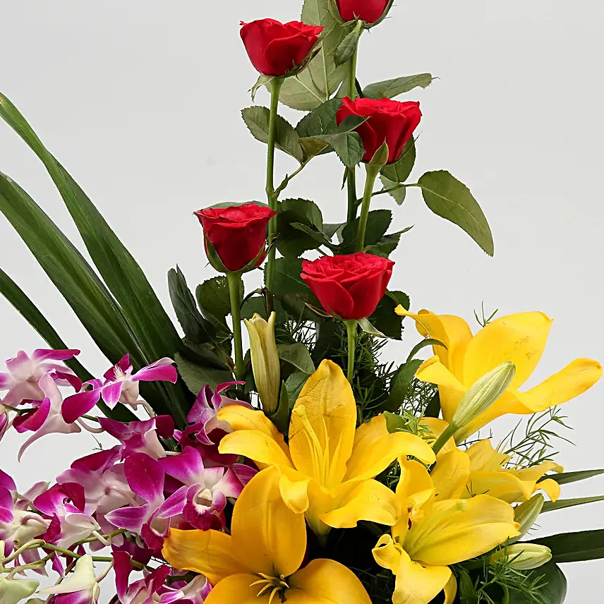 Cane basket arrangement of 5 red roses, 4 purple orchids, 2 yellow asiatic lilies and draceane leaves