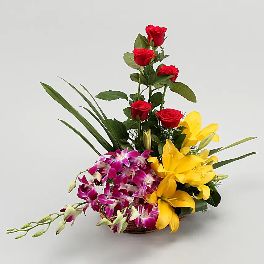 Cane basket arrangement of 5 red roses, 4 purple orchids, 2 yellow asiatic lilies and draceane leaves