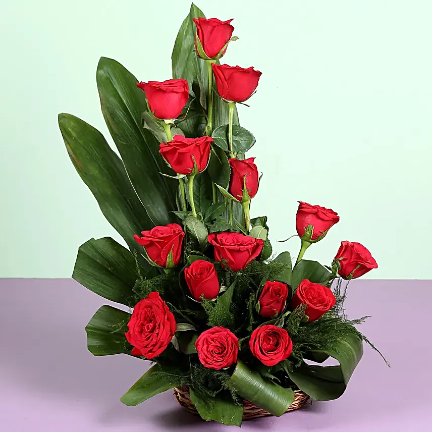 Cane basket arrangement of 15 red roses, draceane leaves and seasonal filler