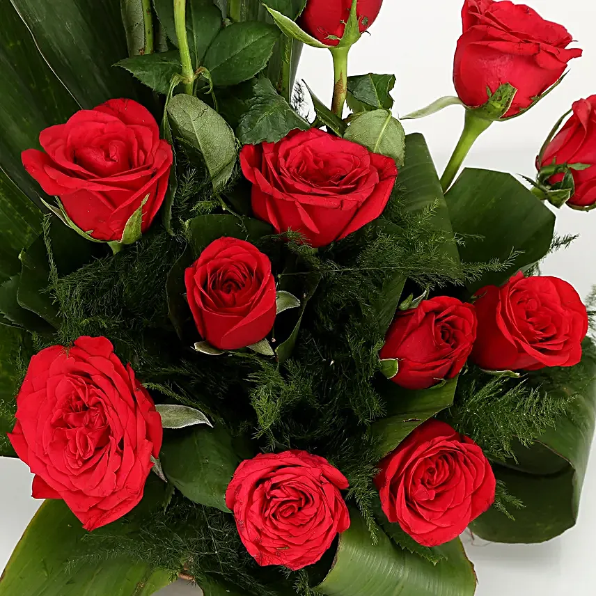 Cane basket arrangement of 15 red roses, draceane leaves and seasonal filler
