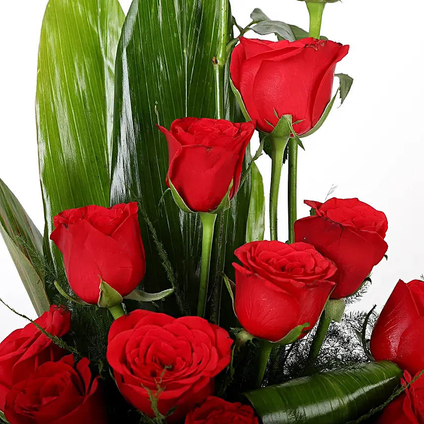 Cane basket arrangement of 15 red roses, draceane leaves and seasonal filler