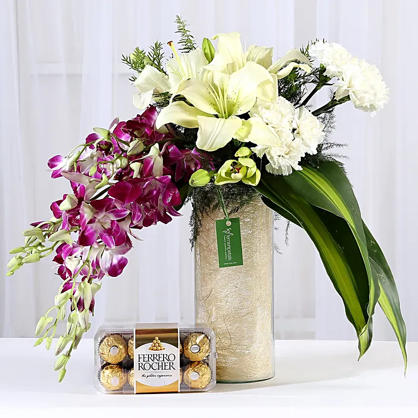 Combo of a glass vase arrangement of 6 purple orchids, 3 white asiatic lilies, 6 white carnations, draceane leaves and vase filler, with 16 pieces of ferrero rocher chocolates