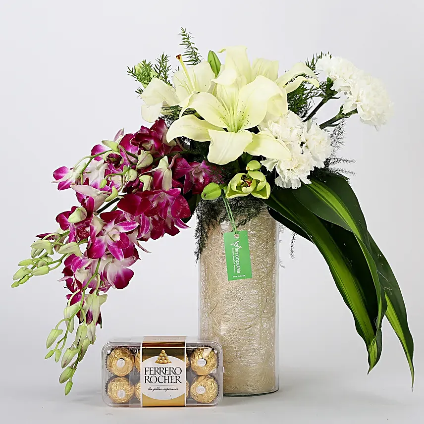 Combo of a glass vase arrangement of 6 purple orchids, 3 white asiatic lilies, 6 white carnations, draceane leaves and vase filler, with 16 pieces of ferrero rocher chocolates