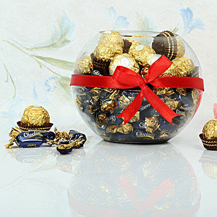 Ferrero rocher and cadbury chocolairs gold candies in a glass vase wrapped with red ribbon:Candies